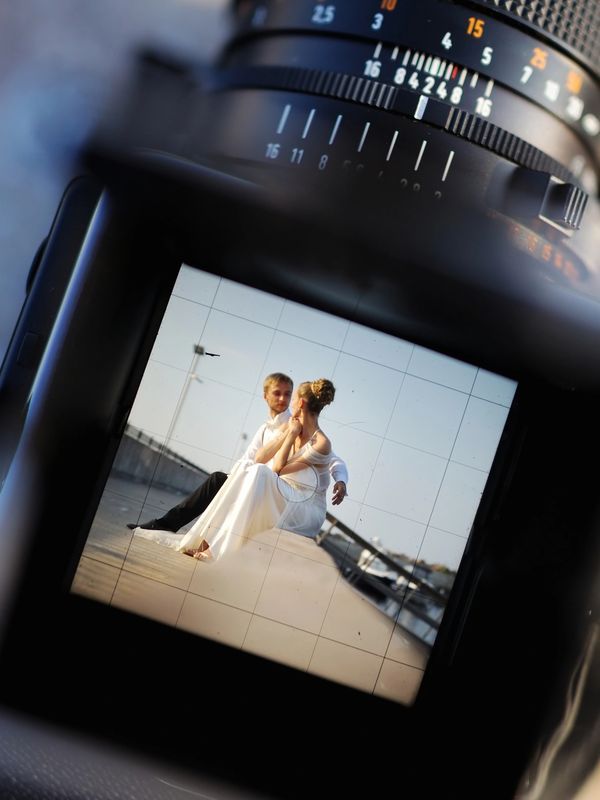 Through a vintage camera viewfinder showing a wedding couple sitting on ledge.