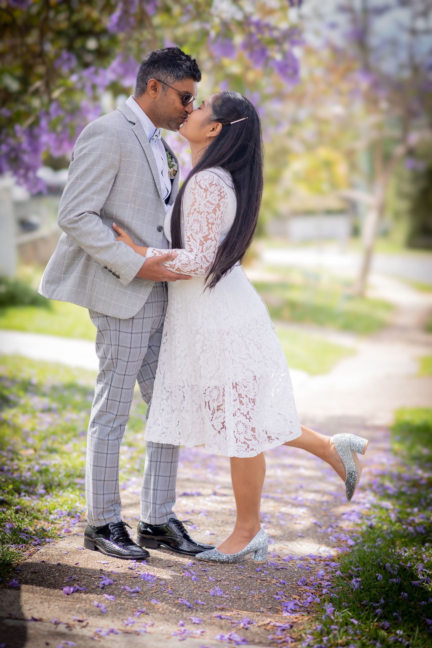 Romantic portrait of couple kissing under flowering trees with purple blossoms.