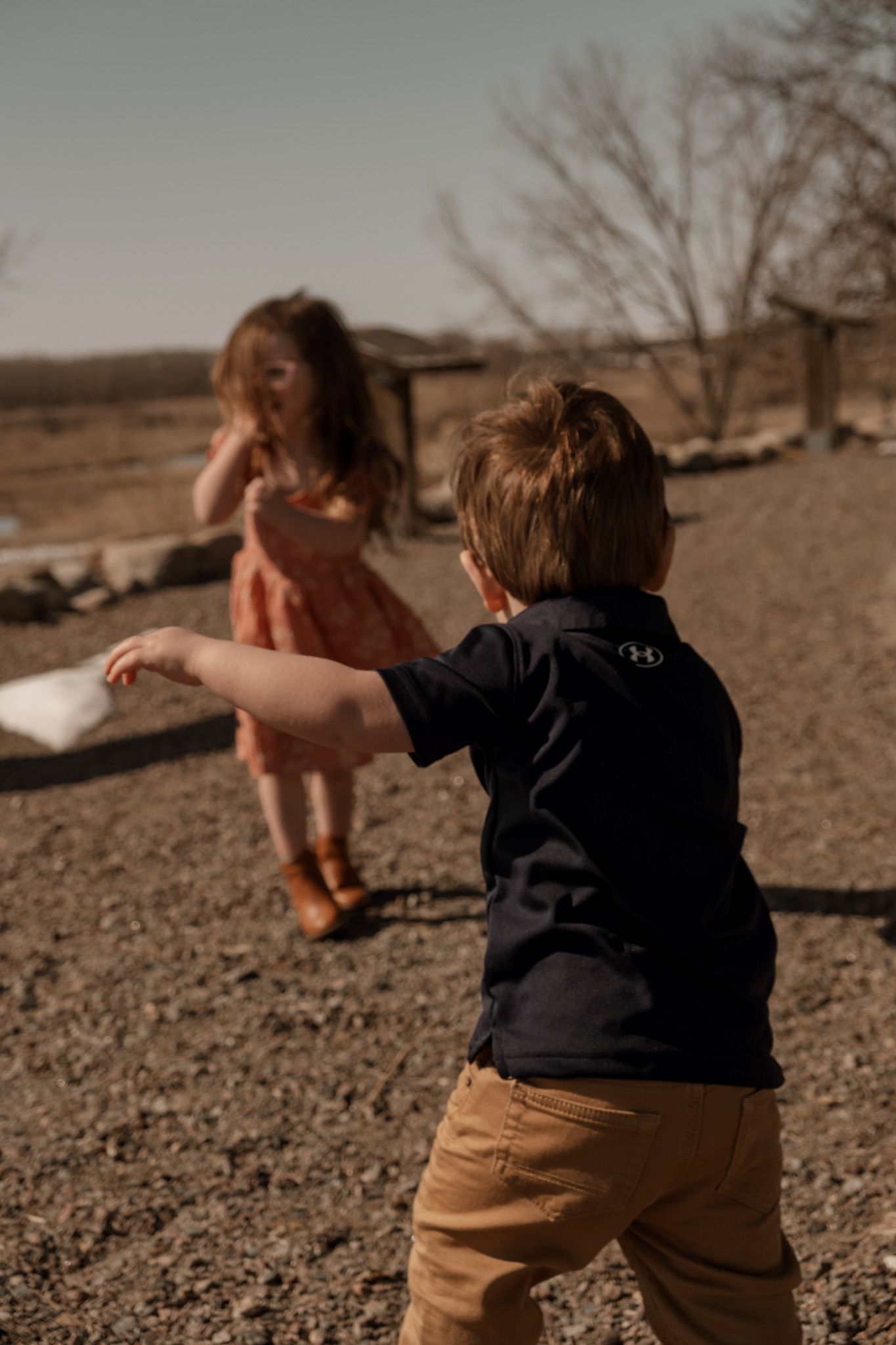 Two young children play together on dry ground during golden hour in a rustic outdoor setting.