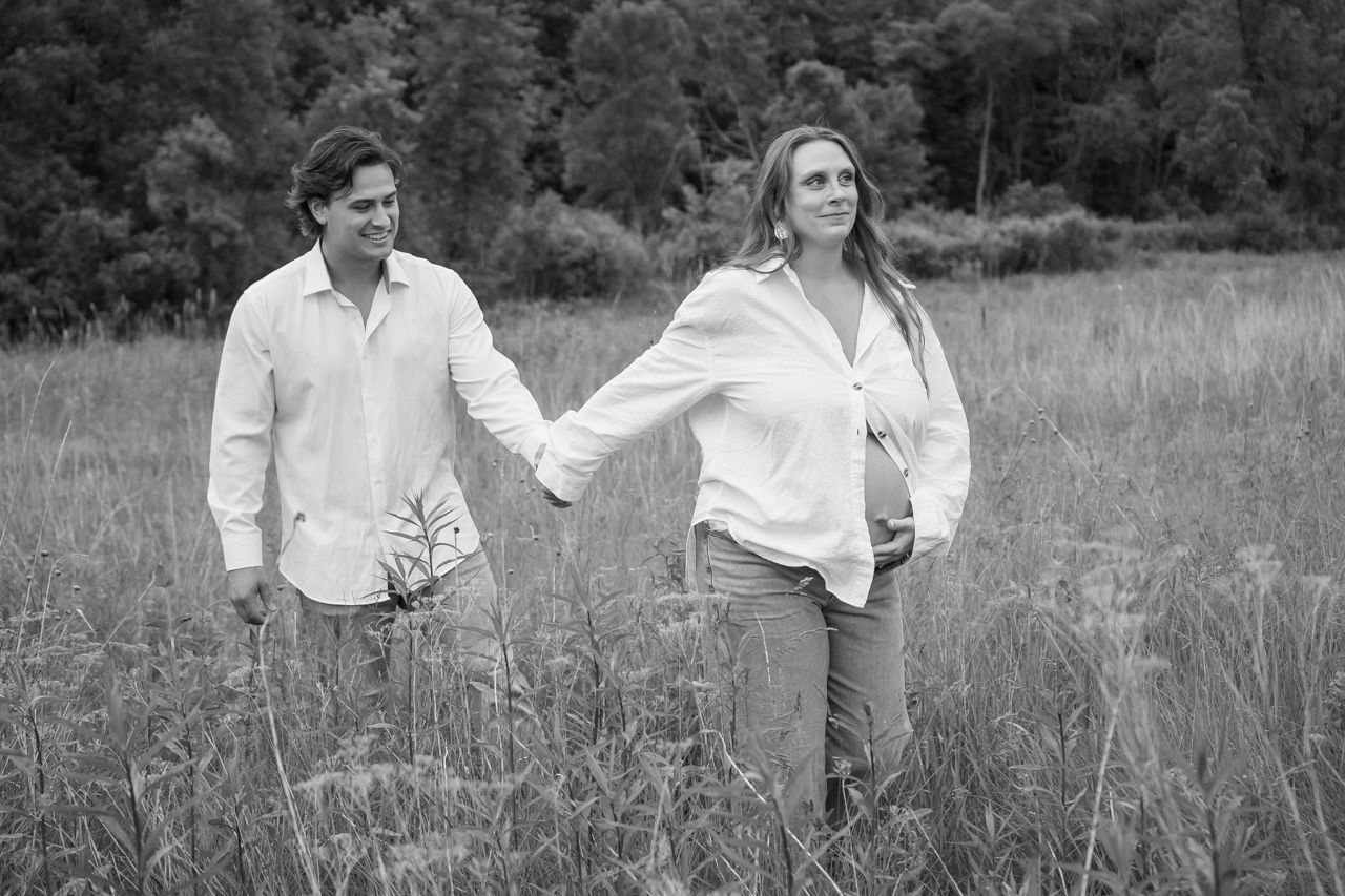 Couple in white shirts walking and laughing together in a sunny meadow with tall grass and trees in black and white.