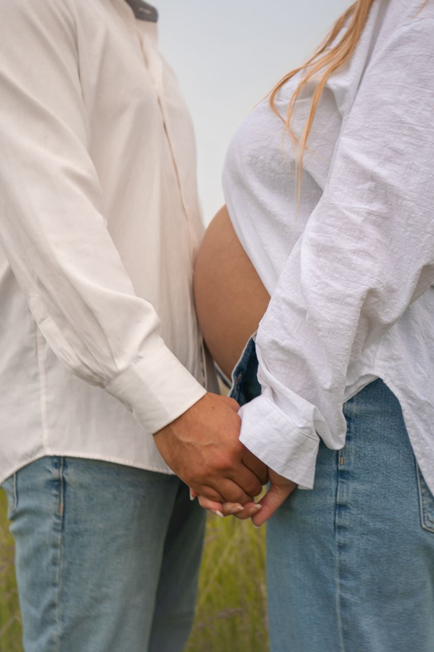Close up of a couple holding hands while wearing casual white shirts and blue jeans.