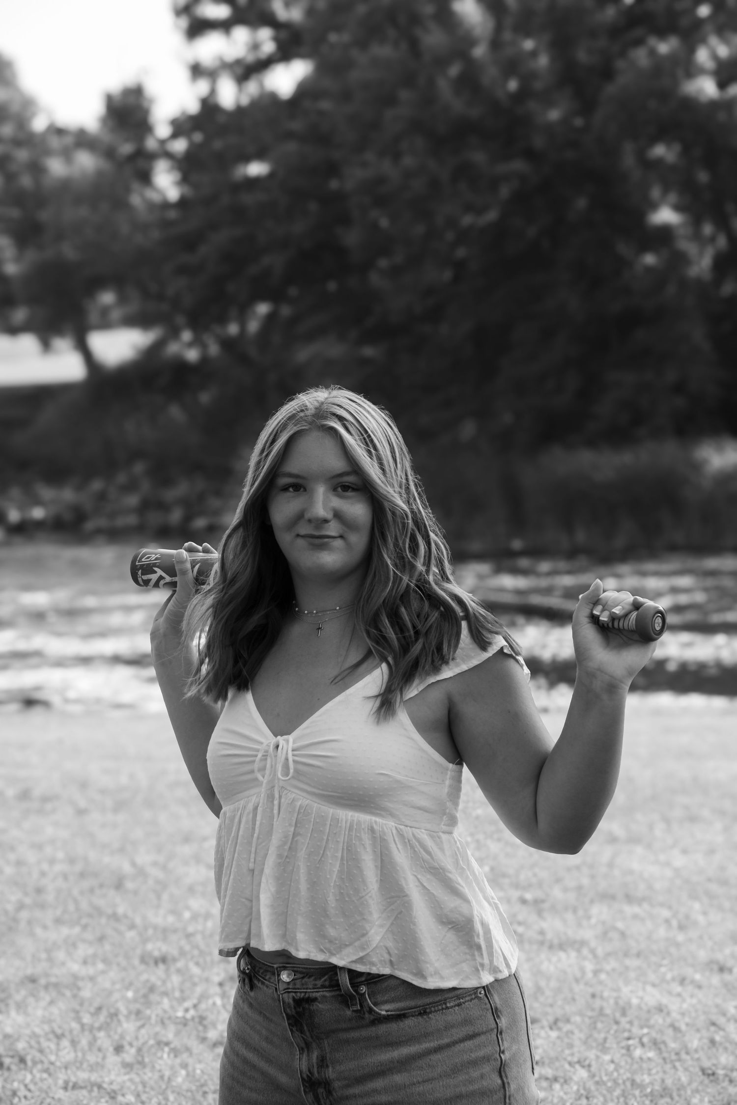 A person in a white top and jeans poses outdoors holds their long hair in a casual black and white portrait.