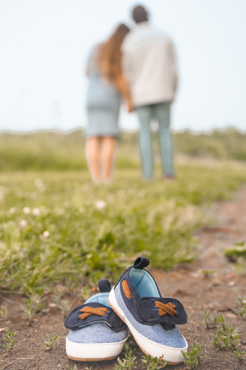 Small sneakers in foreground with blurred couple holding hands on grassy path in background.