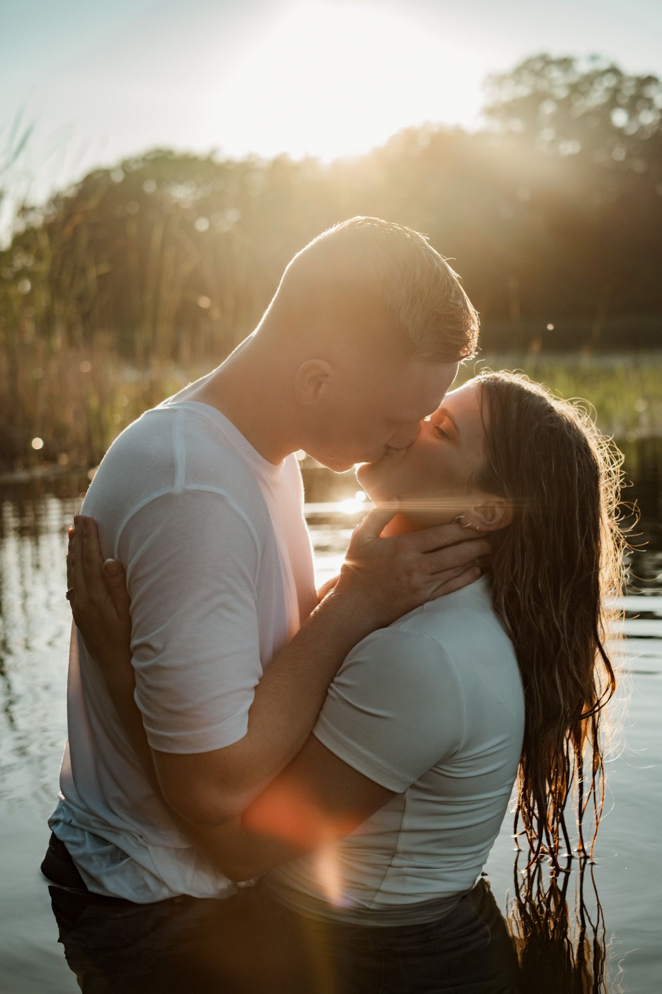 A couple in white shirts share an intimate moment by the water during golden hour sunset.