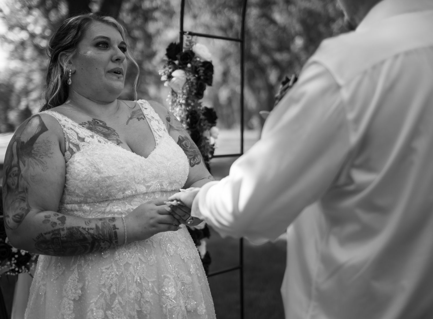 A black and white photo captured during a wedding ceremony with the bride wearing a lace gown exchanging vows.