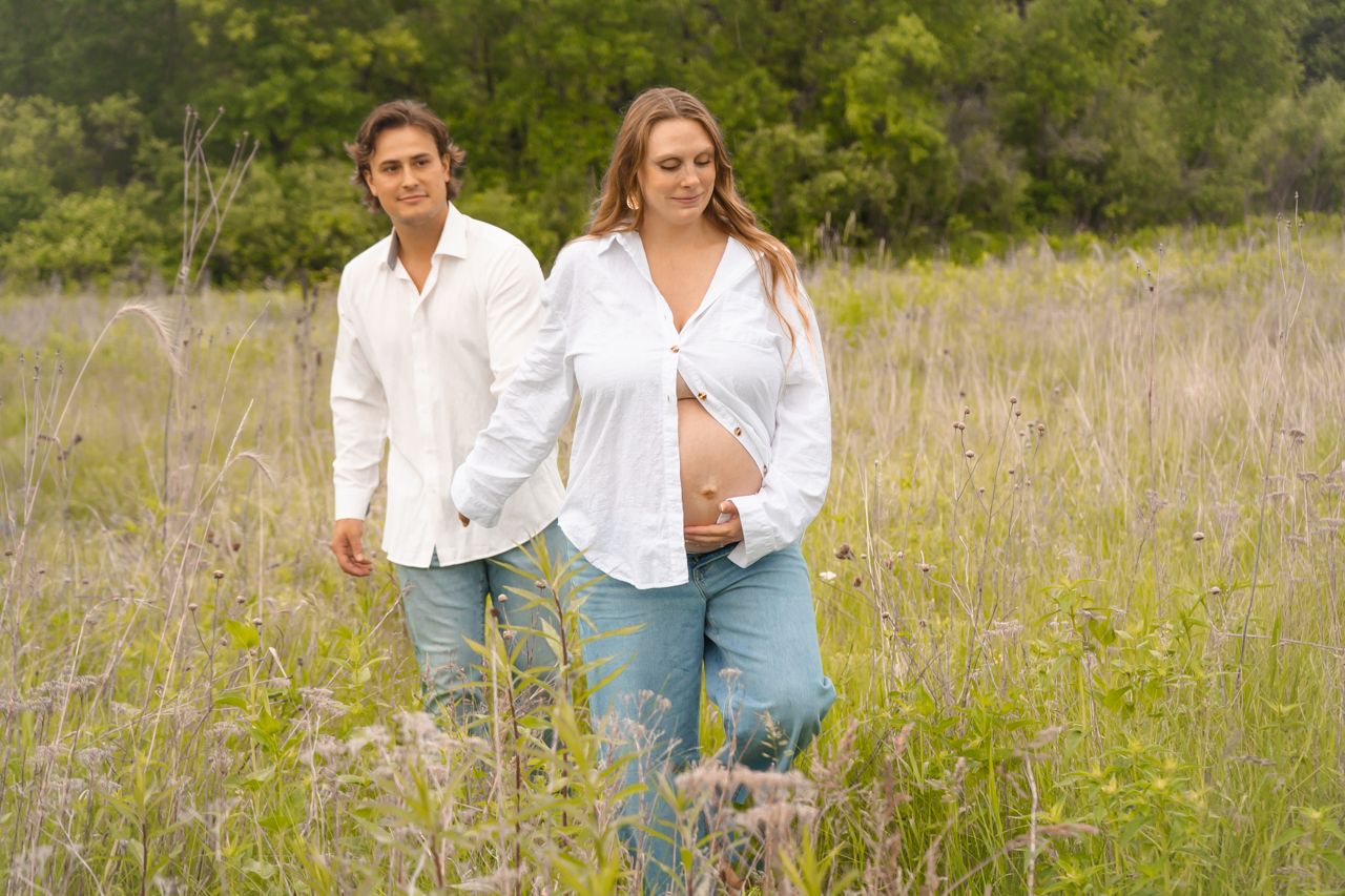 Couple dressed in white and denim enjoying a casual stroll through a summer field of wildflowers.