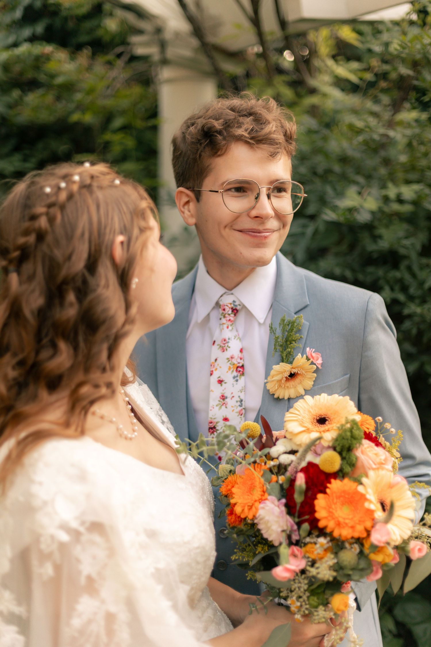 Smiling groom in blue suit with floral tie holding colorful bridal bouquet.
