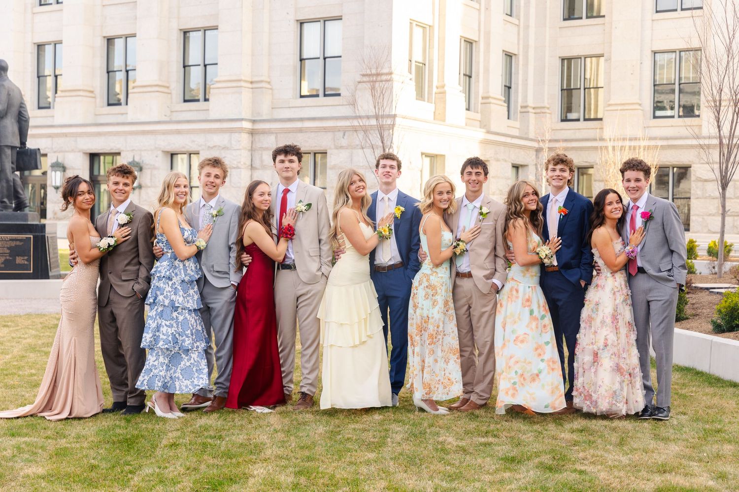 Large group of teens in formal prom attire posing together outside a government building.