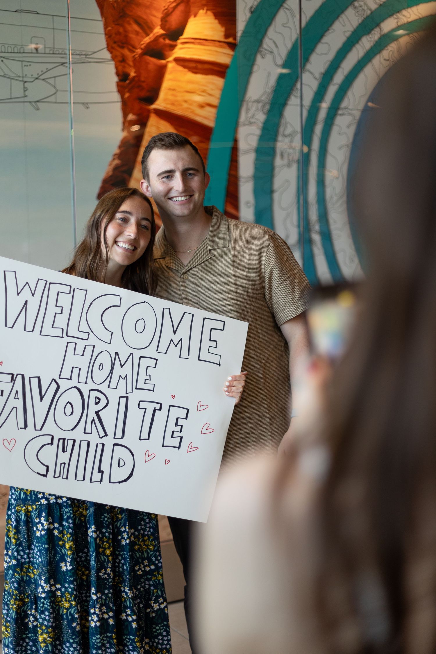 Couple posing with a Welcome Home Favorite Child sign being photographed indoors.