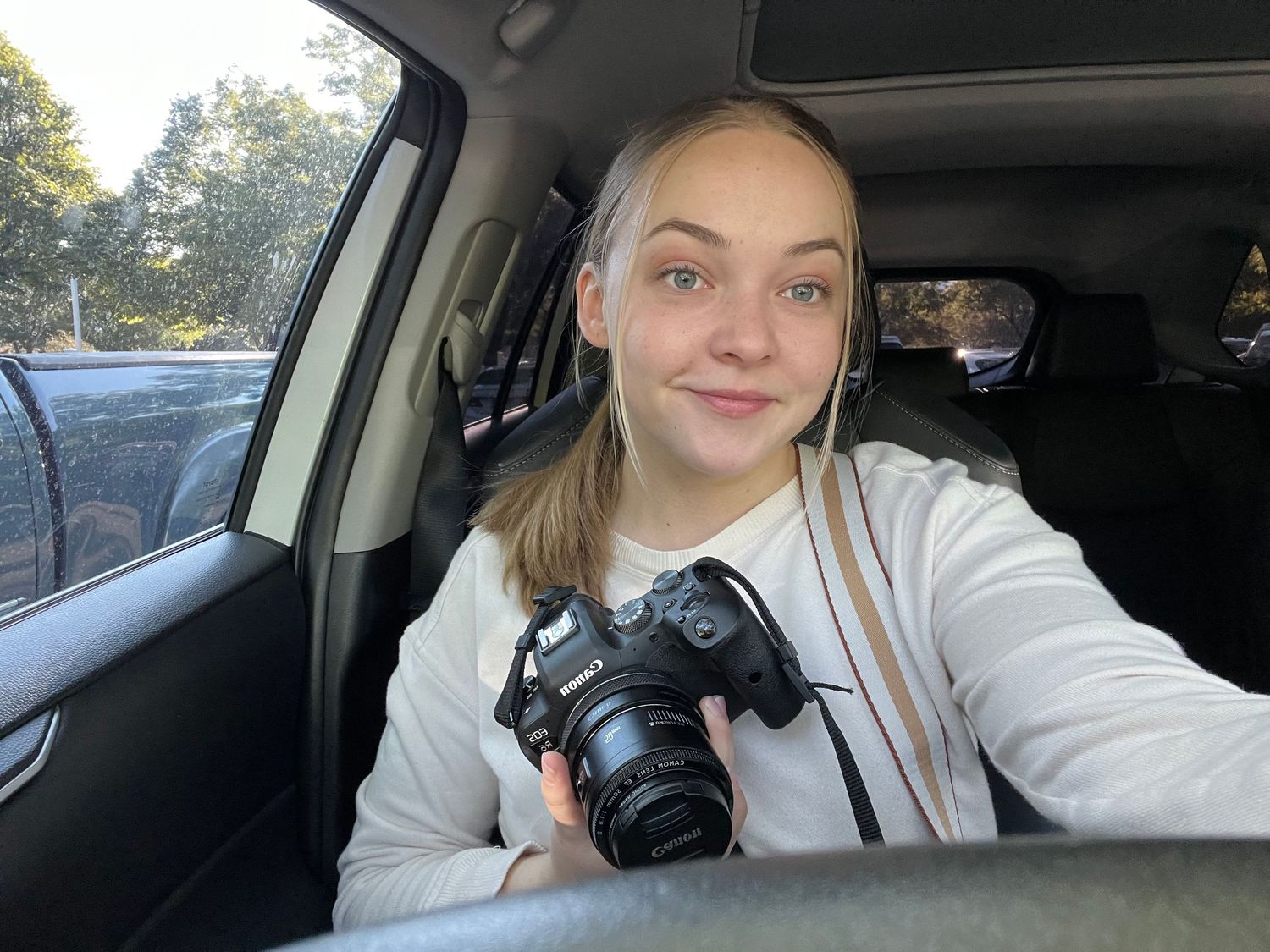 Smiling young woman holds a camera camera while sitting in the backseat of a car.
