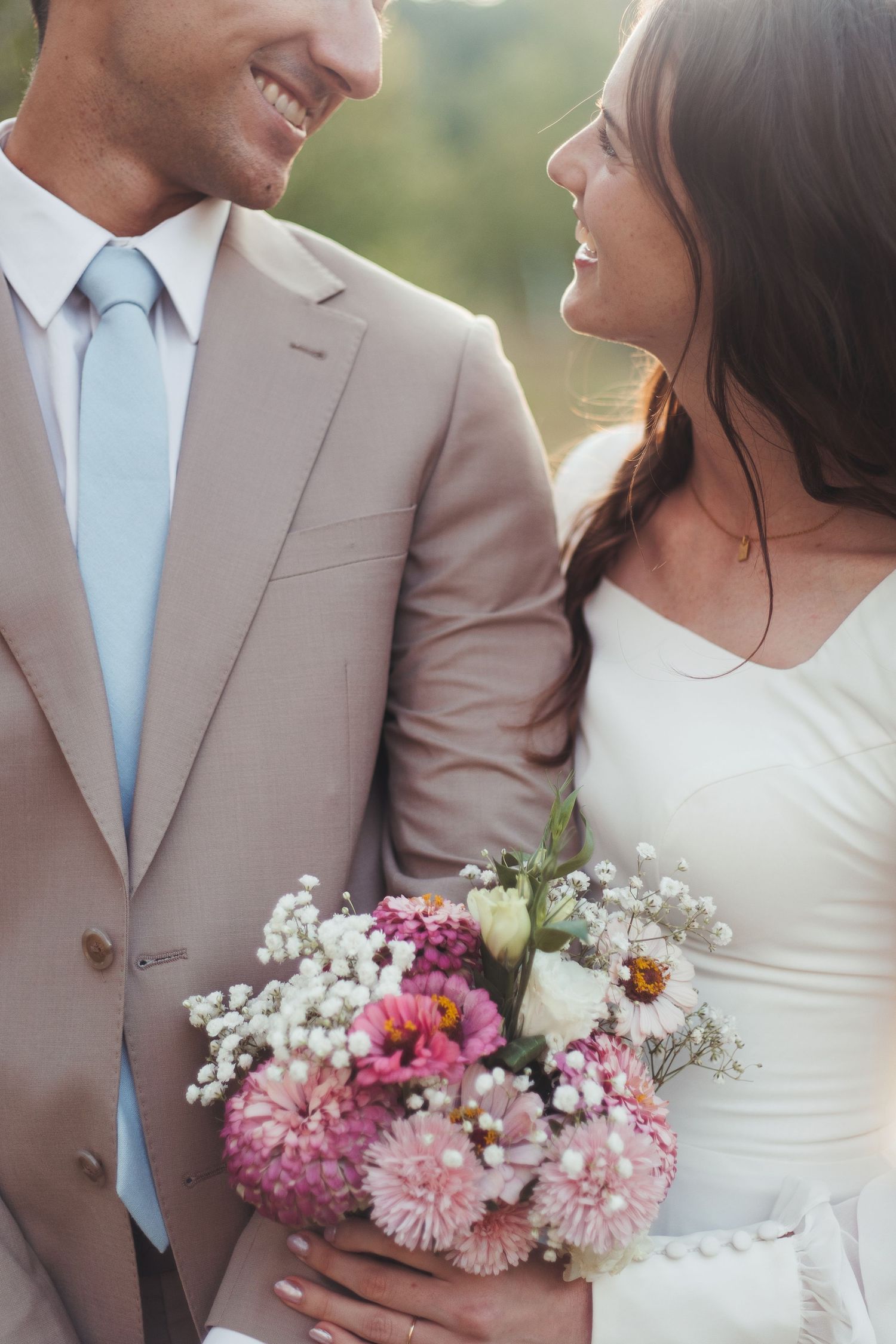 Bride and groom smiling at each other holding a pink and white wedding bouquet.