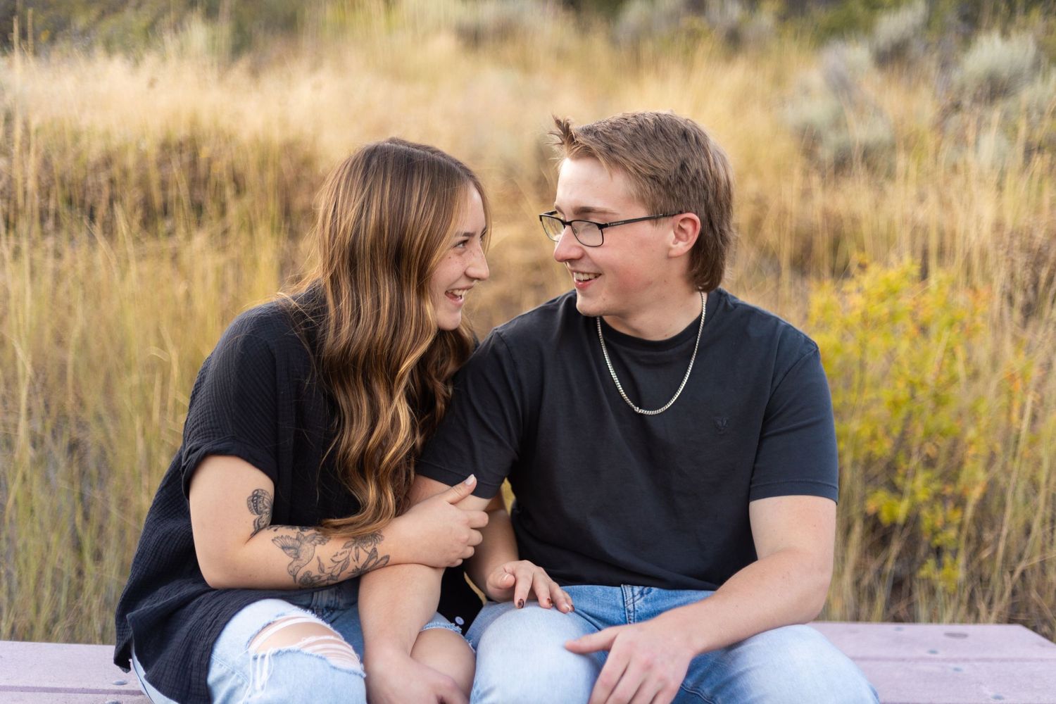 Smiling couple sitting together outdoors in matching black shirts with golden field background.