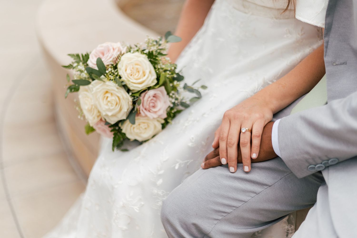 Bride and groom holding hands with wedding bouquet of pink and white roses on their special day.