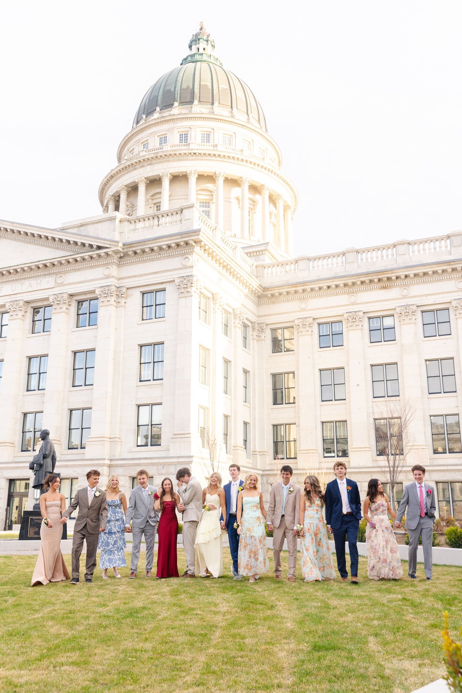 Large prom group in formal attire posing on lawn in front of a grand capitol building.