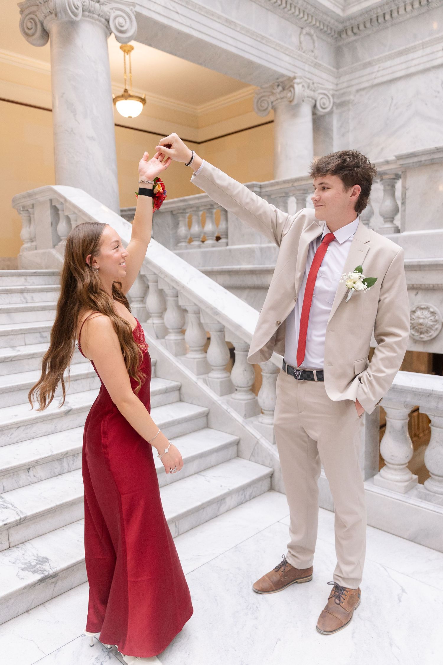 Teenage couple dancing on marble staircase, girl in red gown and boy in tan suit with red tie.