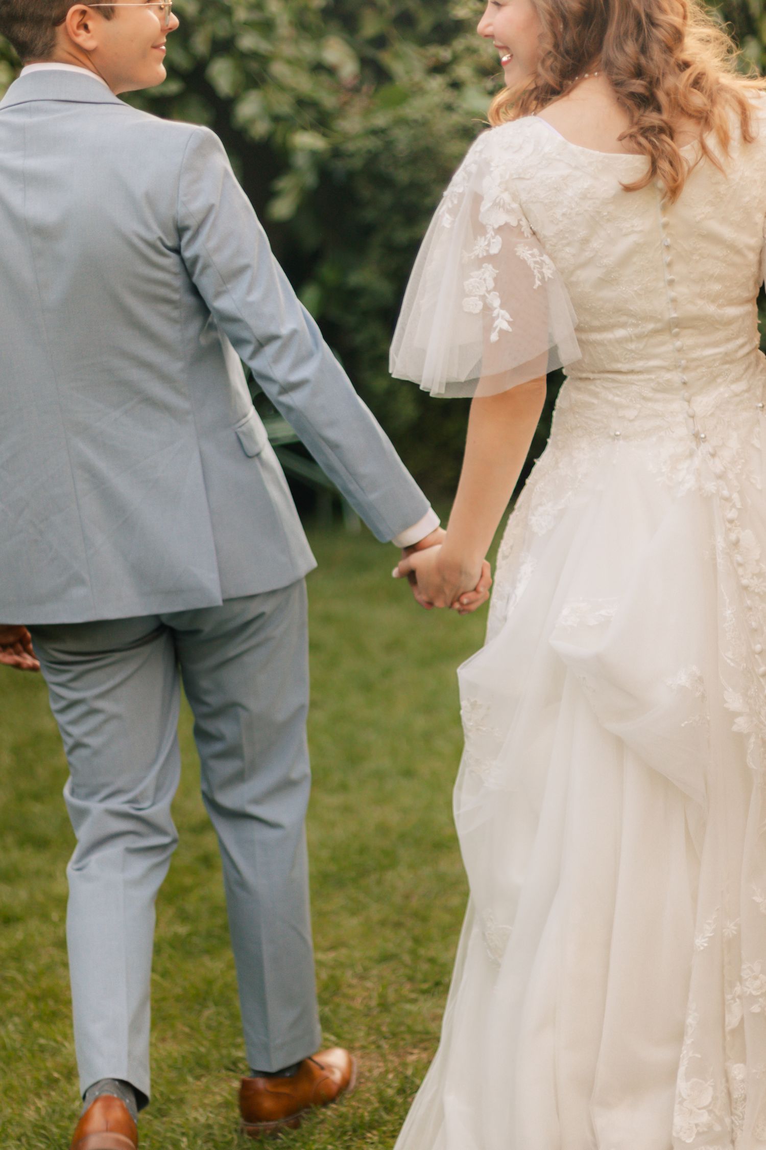 Bride and groom holding hands walking through green garden after ceremony.