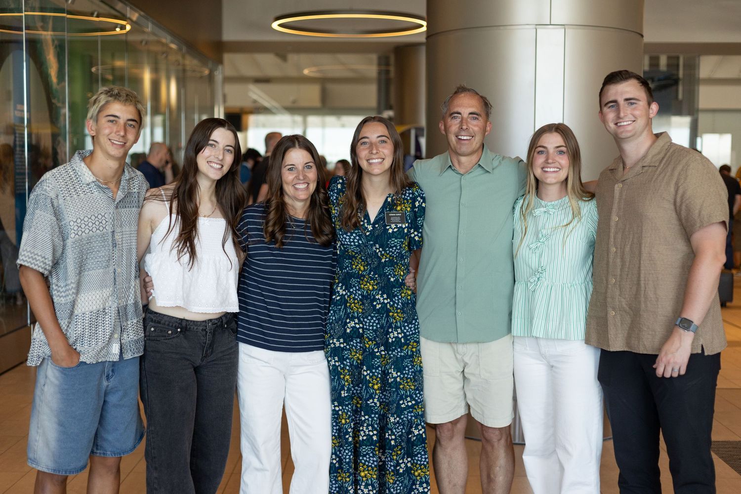 Cheerful family of seven poses together smiling inside a bright modern venue at a special event.