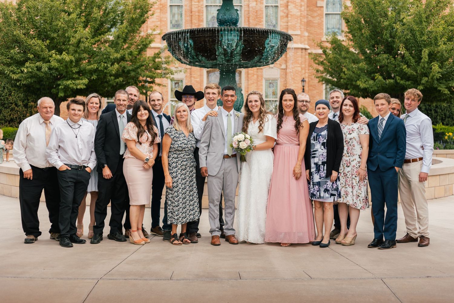 Wedding group photo with bride and groom surrounded by family and friends in front of a decorative fountain.