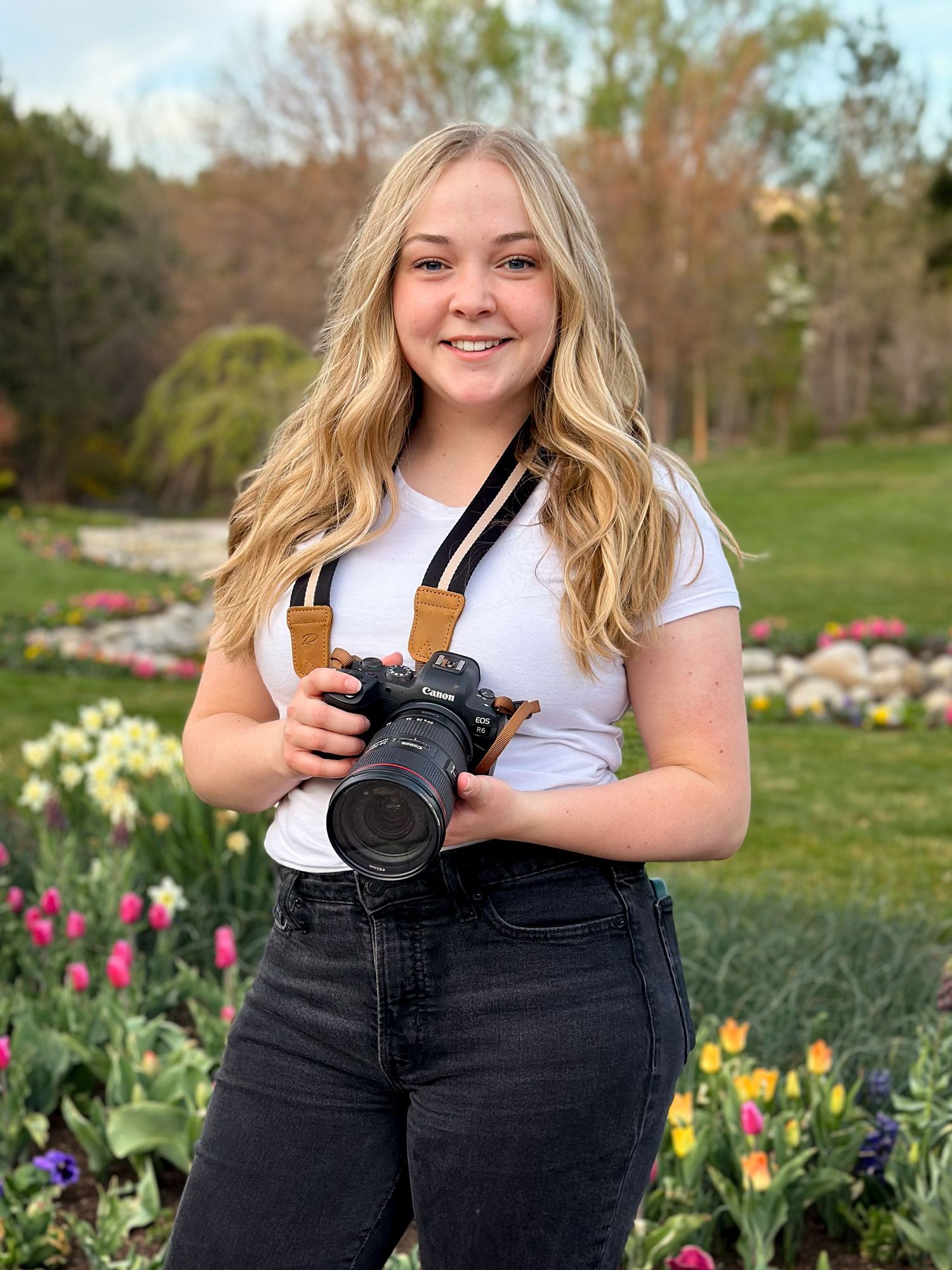 Kaylee Anne holds a camera in a colorful tulip garden outdoors.