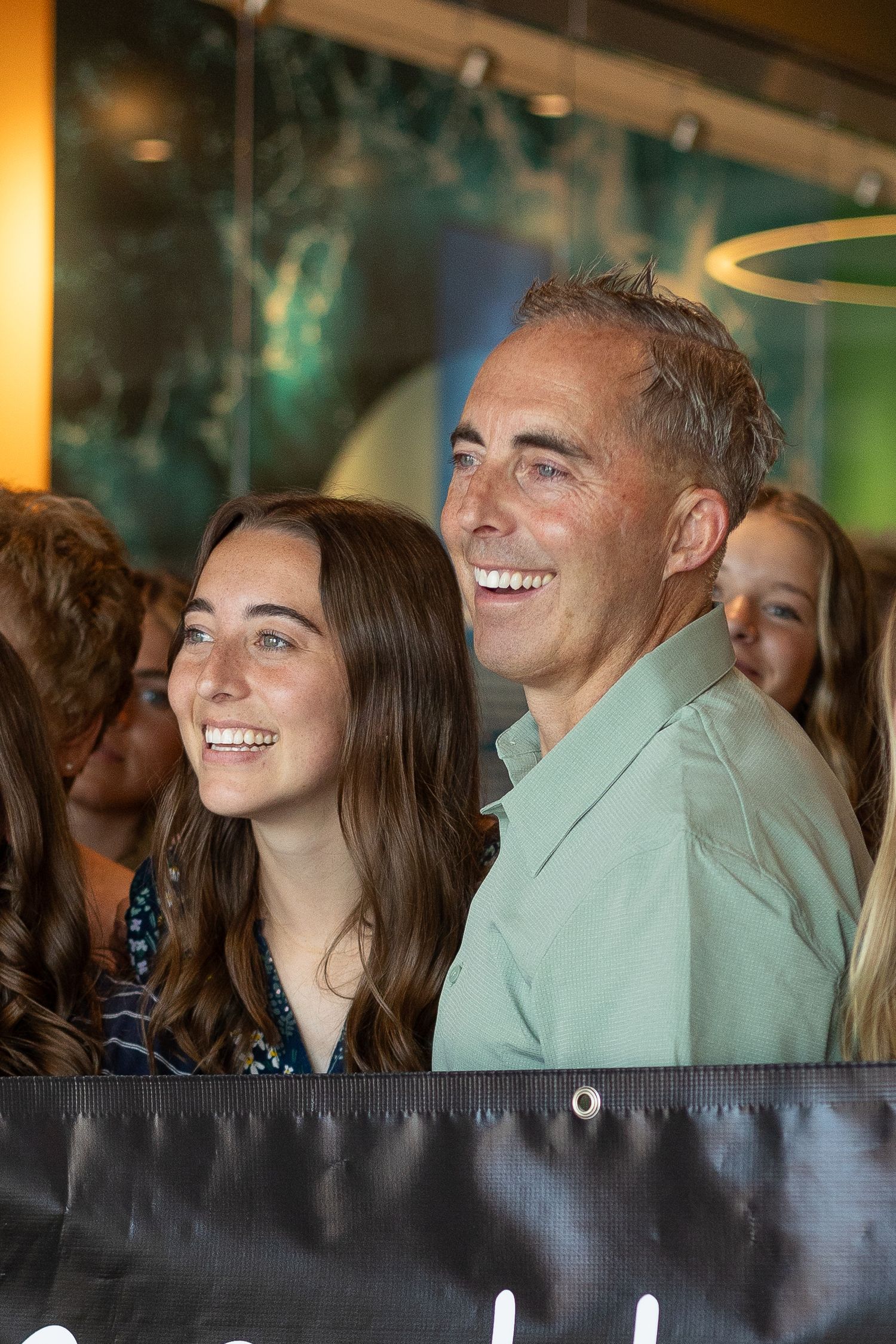 Smiling young woman and her dad stand together holding a banner at a missionary homecoming.