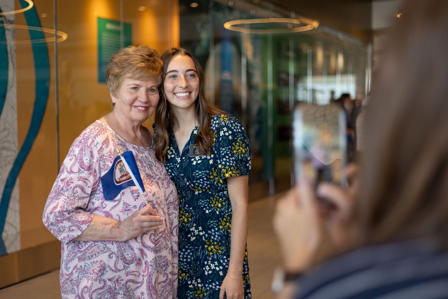 Returned missionary and her grandmother pose for a photo while someone captures the moment on a smartphone.