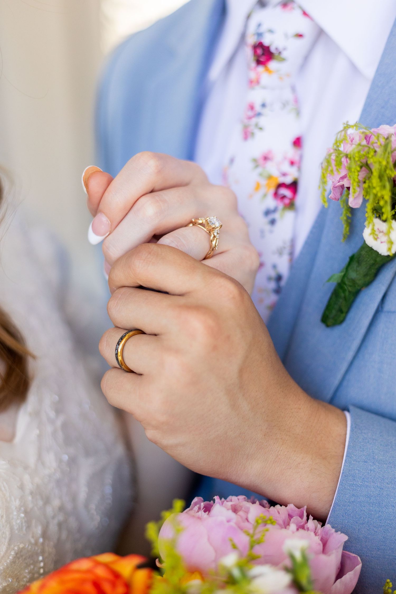 Close-up of bride and groom holding hands showing gold wedding rings with floral boutonniere.