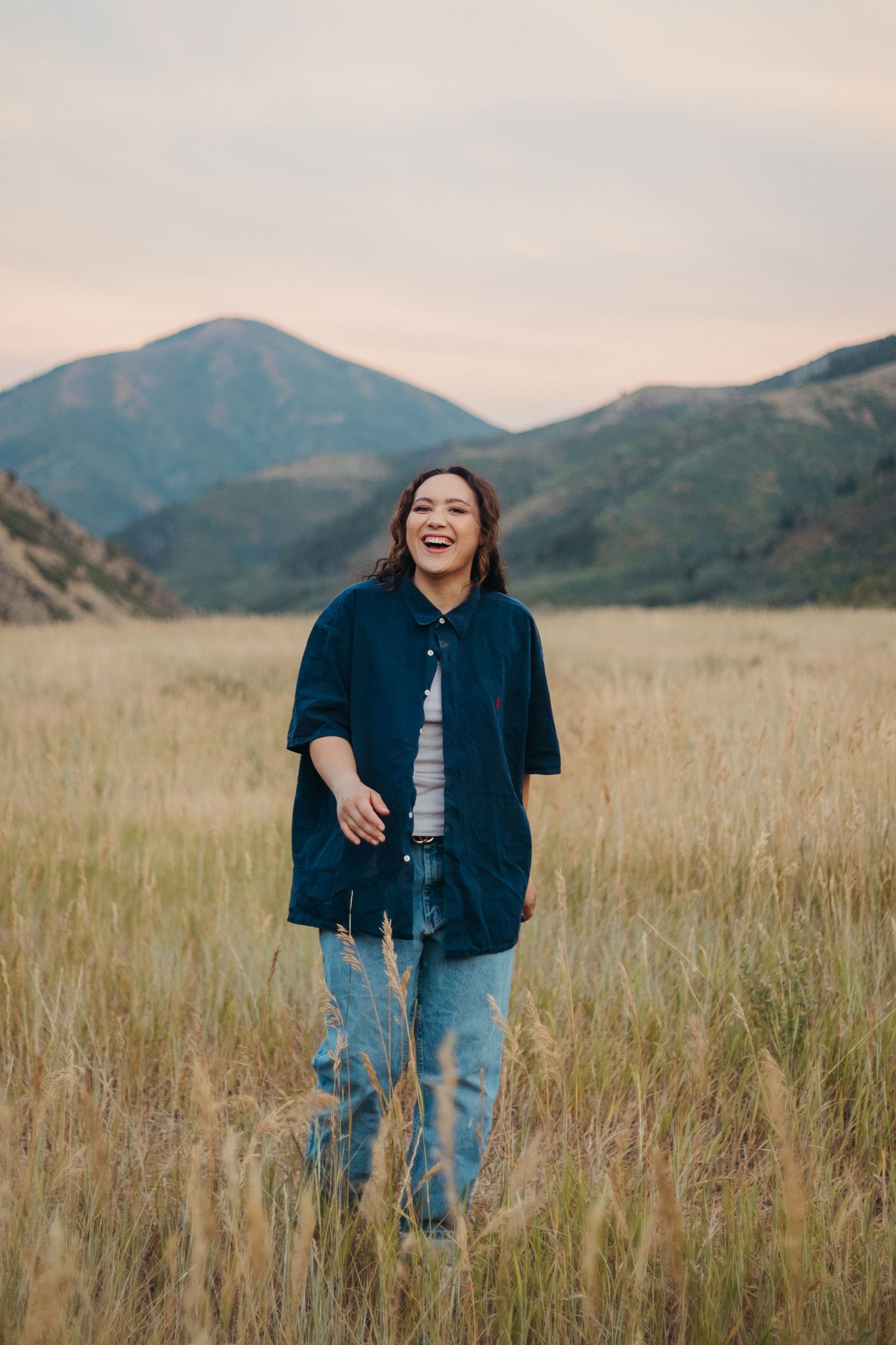 Joyful young woman in navy shirt and jeans laughing while walking through tall golden meadow grass.