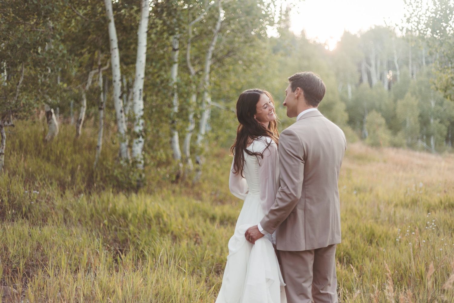 Bride and groom share a romantic moment in a sunlit meadow surrounded by birch trees in autumn.