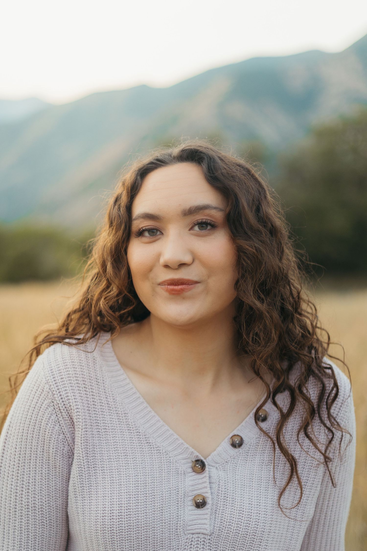 Close portrait of young curly-haired woman in ribbed sweater with mountains in soft background.