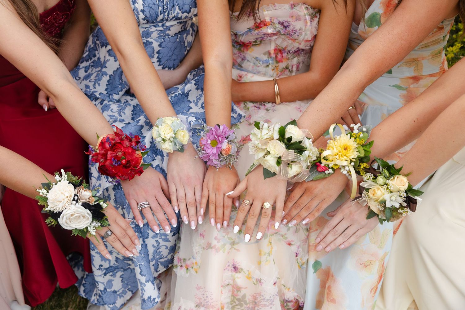 Close-up of young women showing off floral wrist corsages in colorful prom dresses.