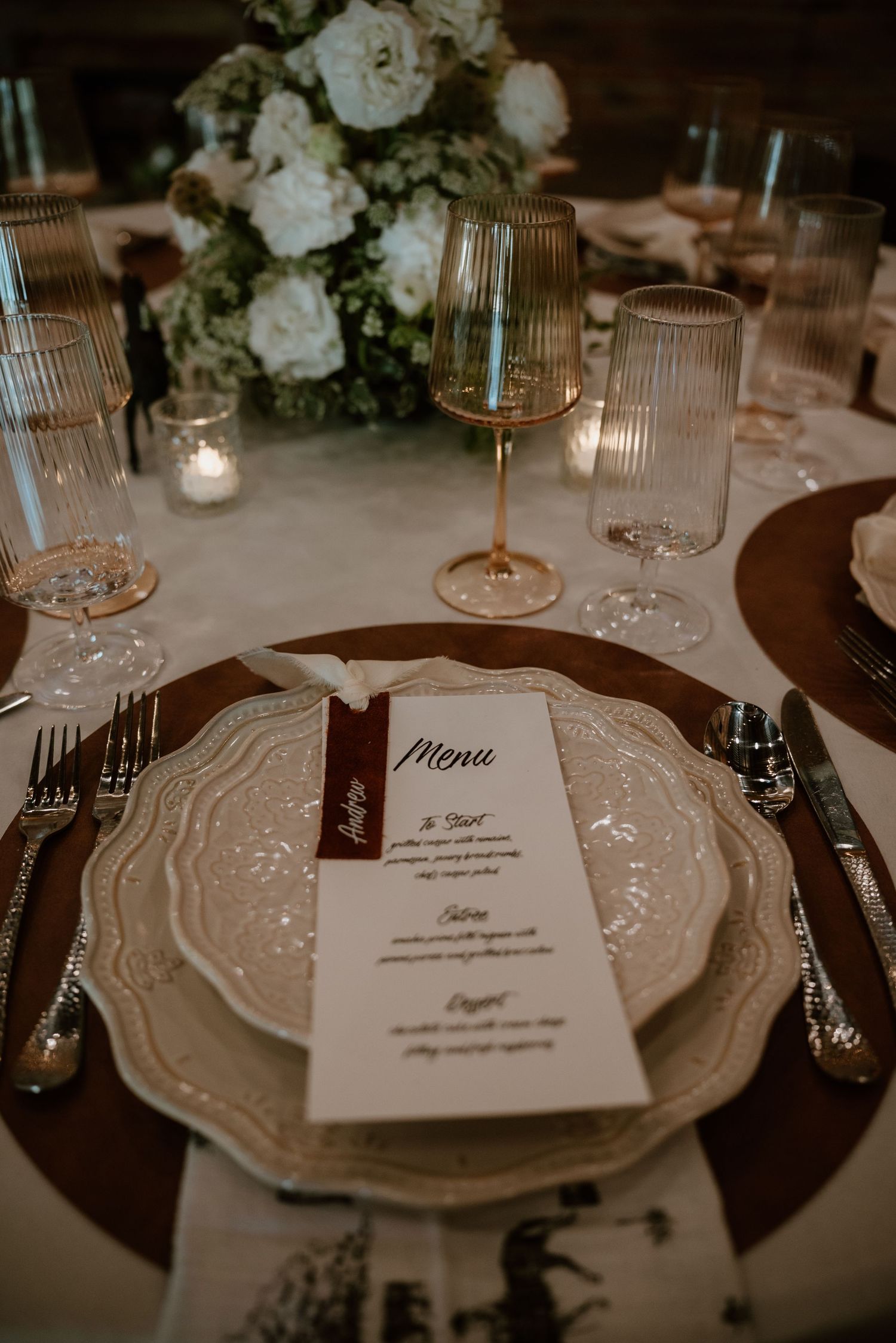 Formal place settings with white plates, menus and crystal glassware at a wedding reception.