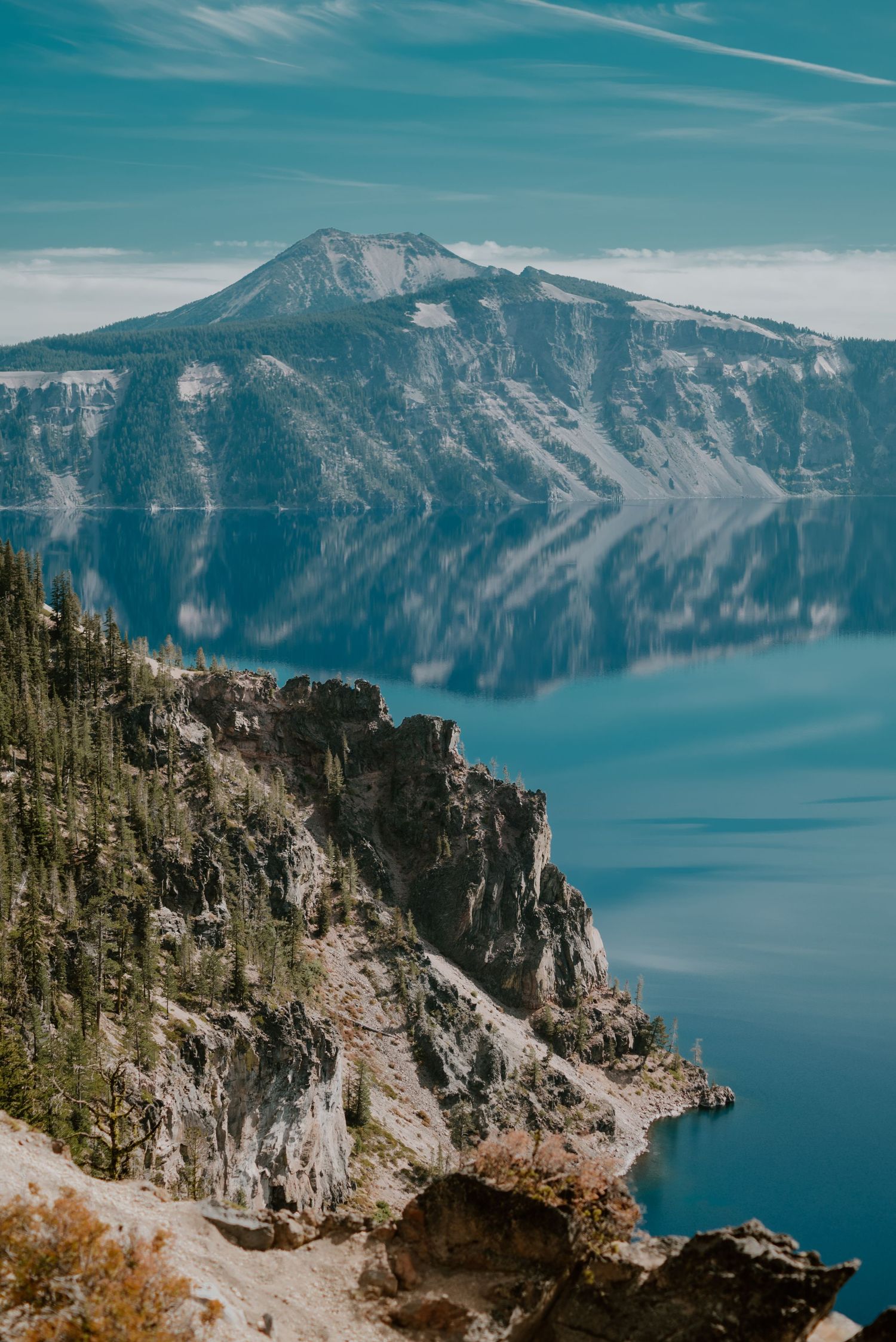 Crater Lake's pristine blue waters reflect steep cliffs and mountain peaks.