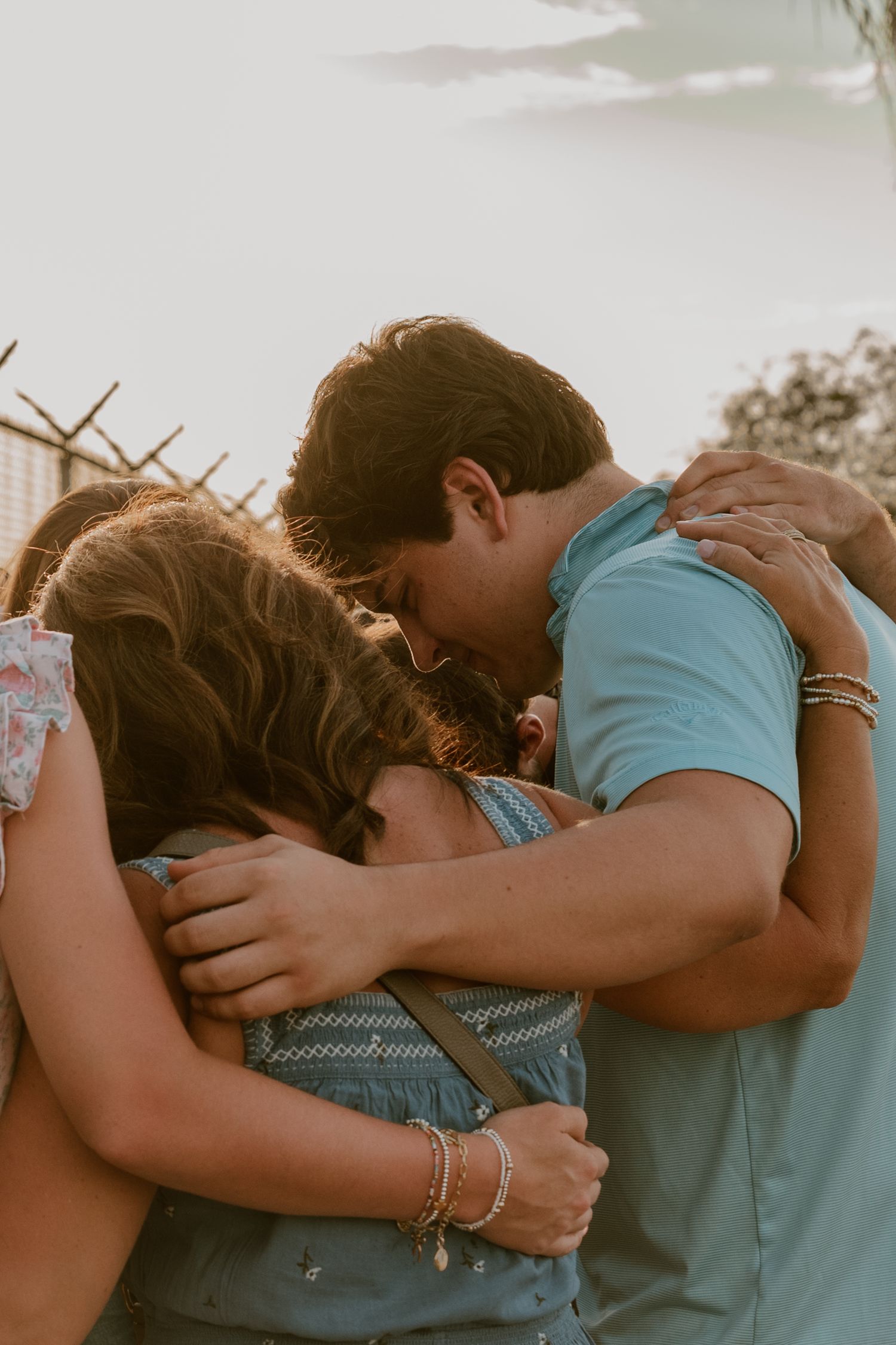 A couple embraces intimately in golden sunlight wearing blue tones.