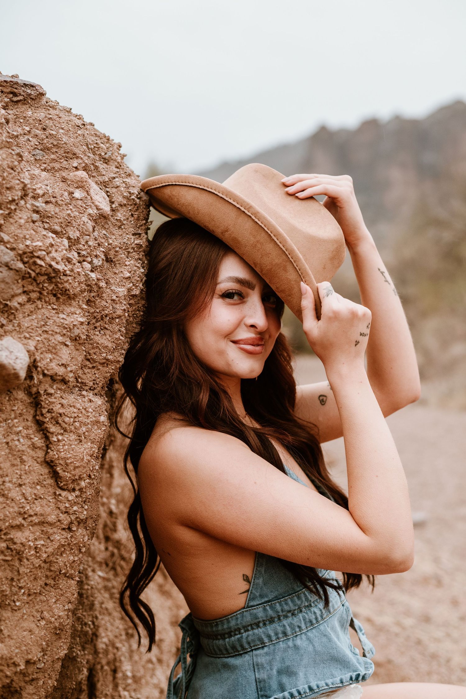 Desert fashion portrait with western hat and sage green top against rocky background.