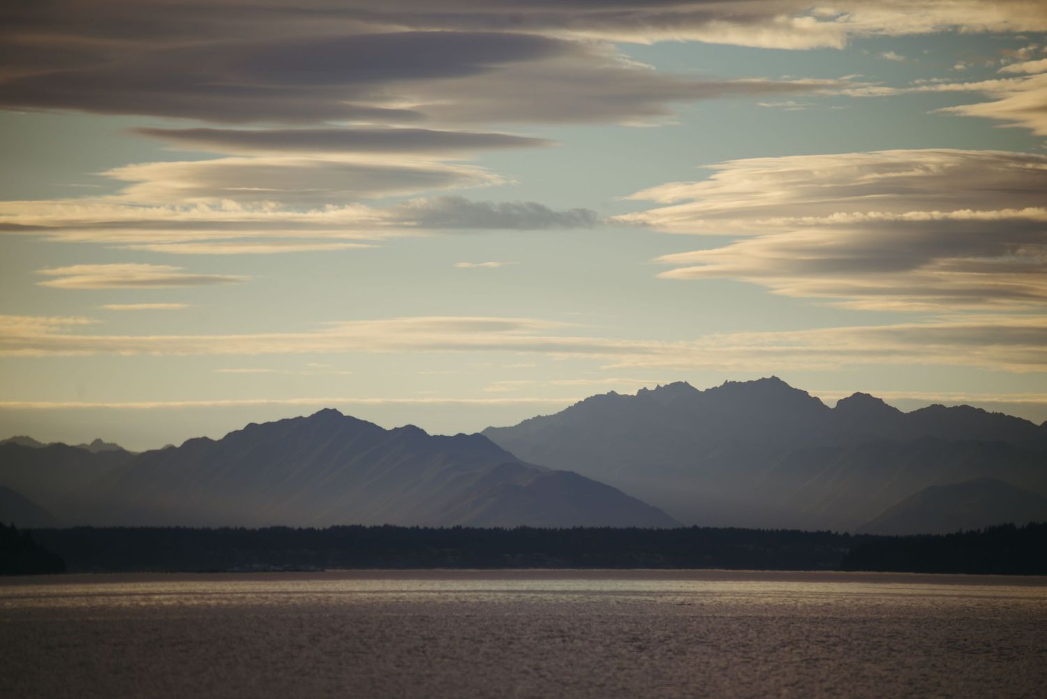 Mountain silhouettes create a dramatic skyline at sunset over a calm lake.
