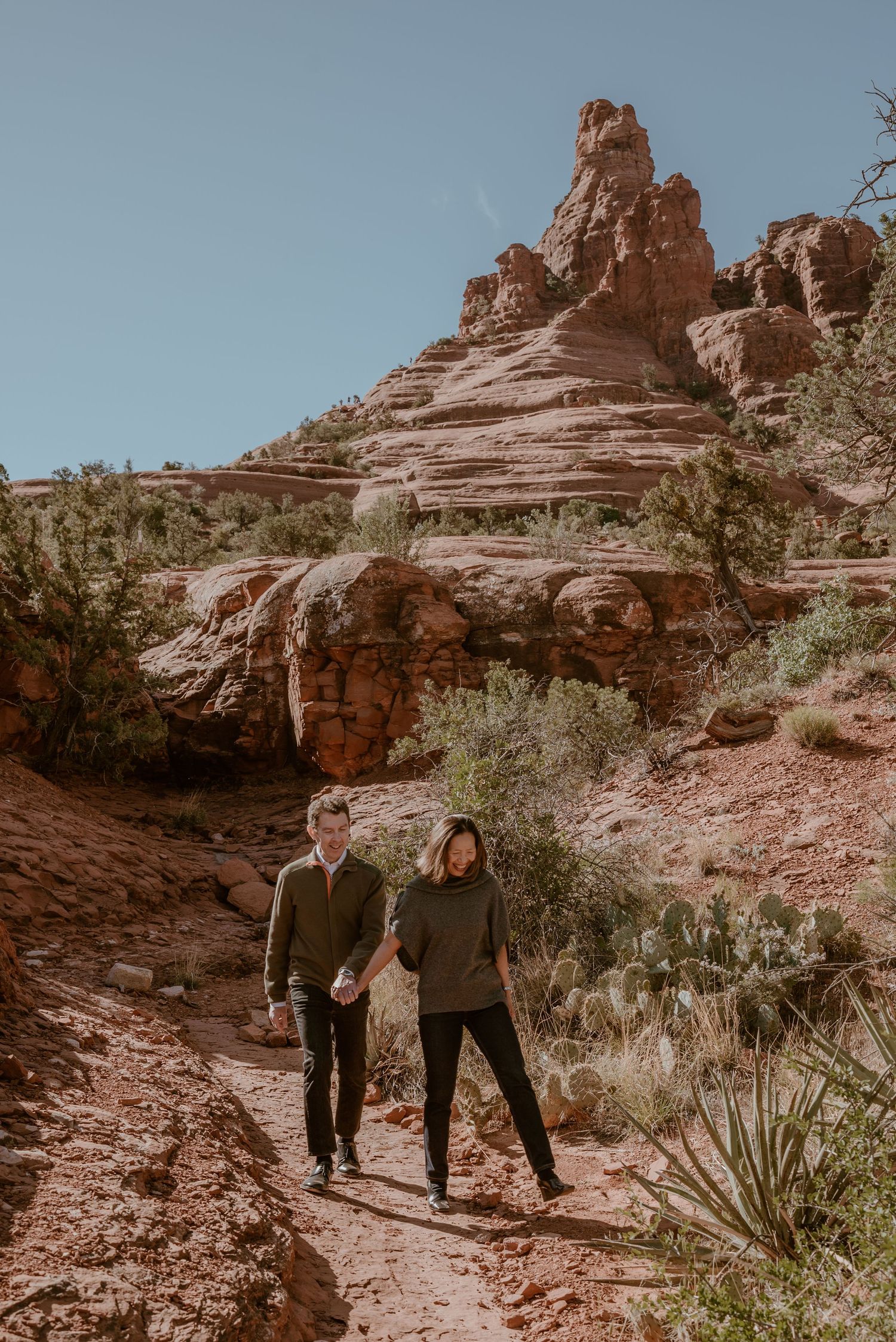 Two people exploring rocky desert terrain with saguaro cacti in the background.