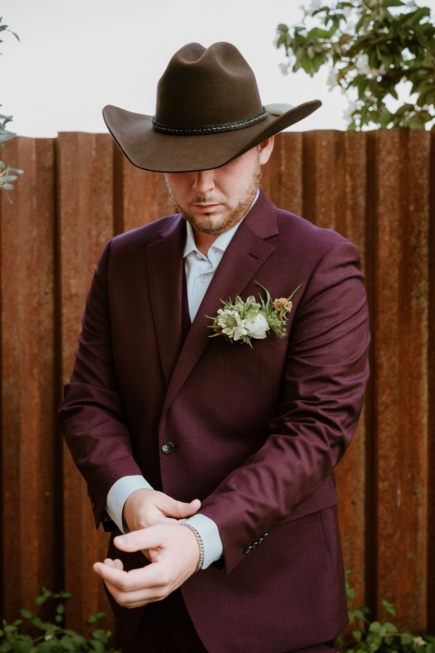 Detail of burgundy suit jacket and brown cowboy hat in western wedding style.
