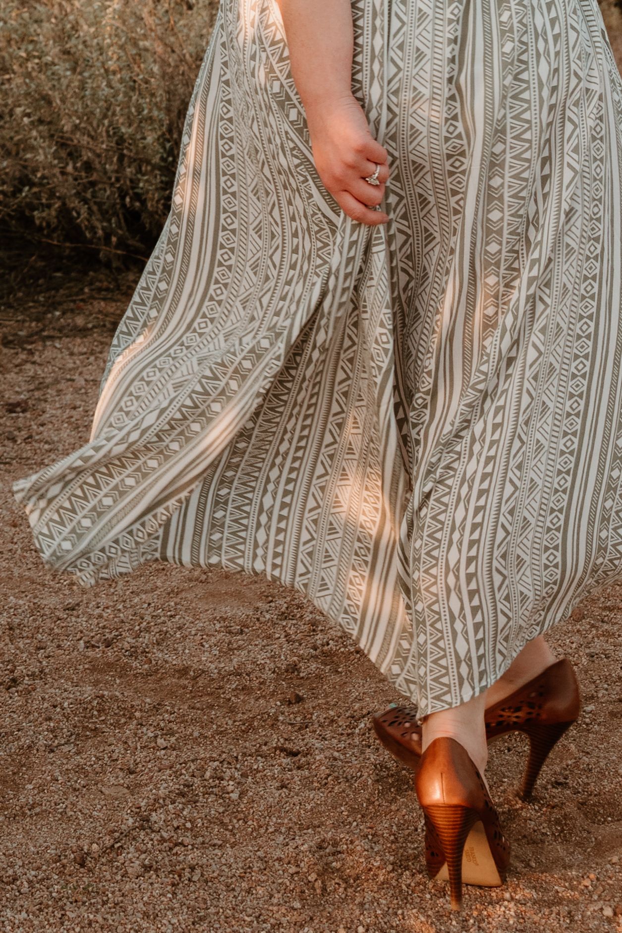 Flowing striped dress fabric and brown high heels walking on desert ground.
