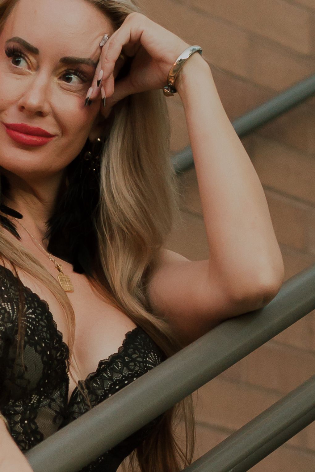 Model in black lace posing near railing in dramatic lighting.