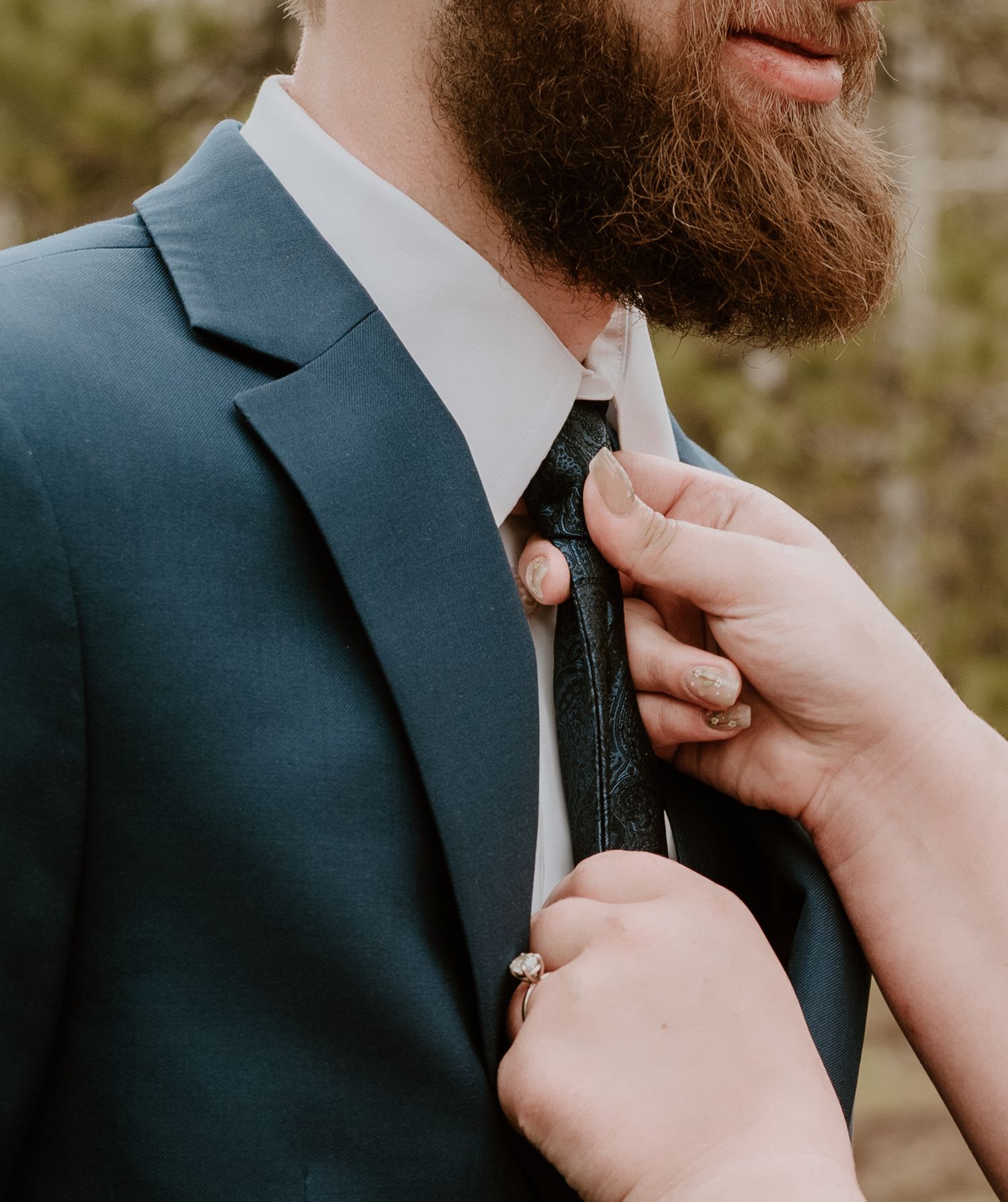 A close-up shot of someone adjusting a black tie against a teal suit jacket.