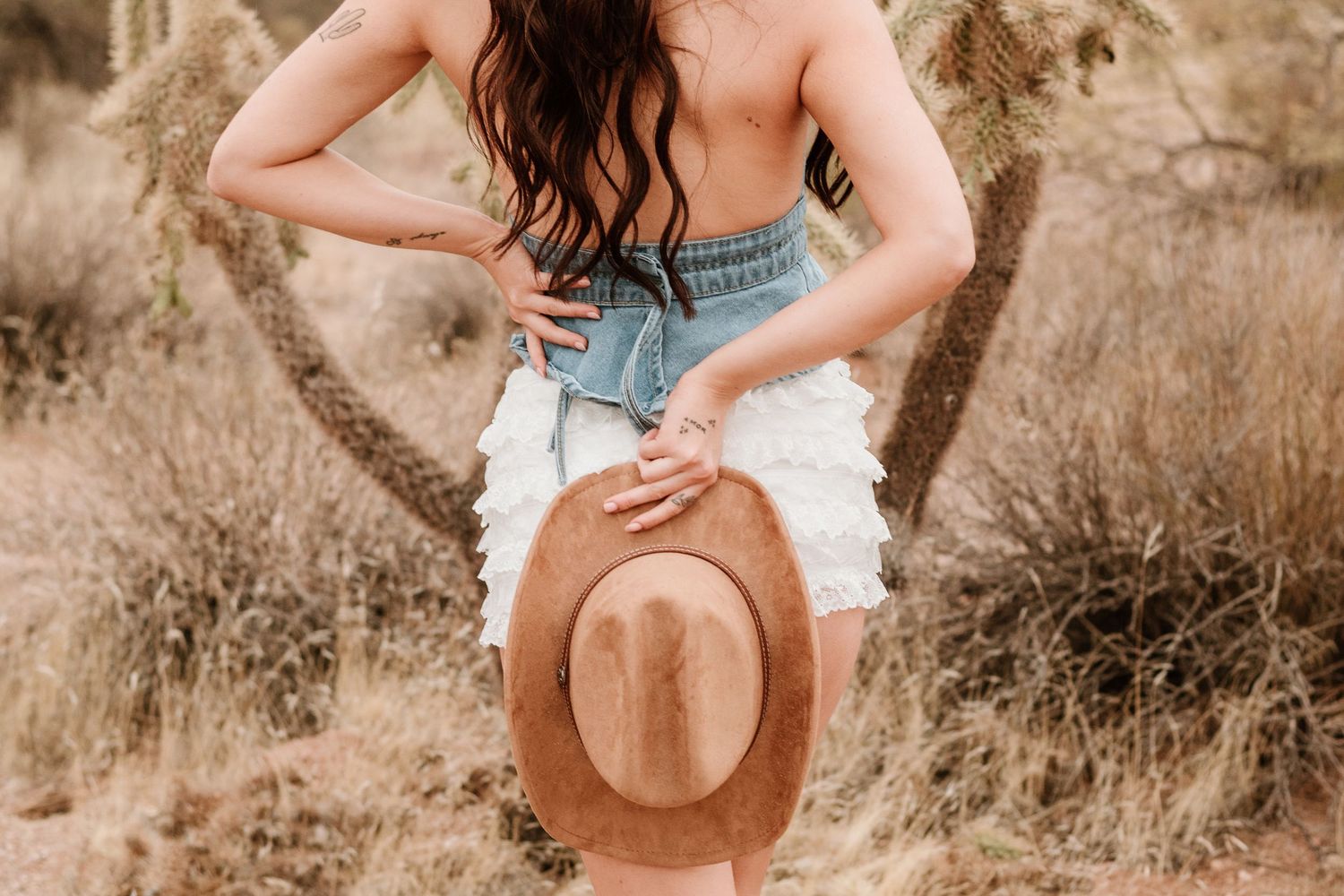Artistic desert photoshoot featuring denim shorts and a brown felt hat.
