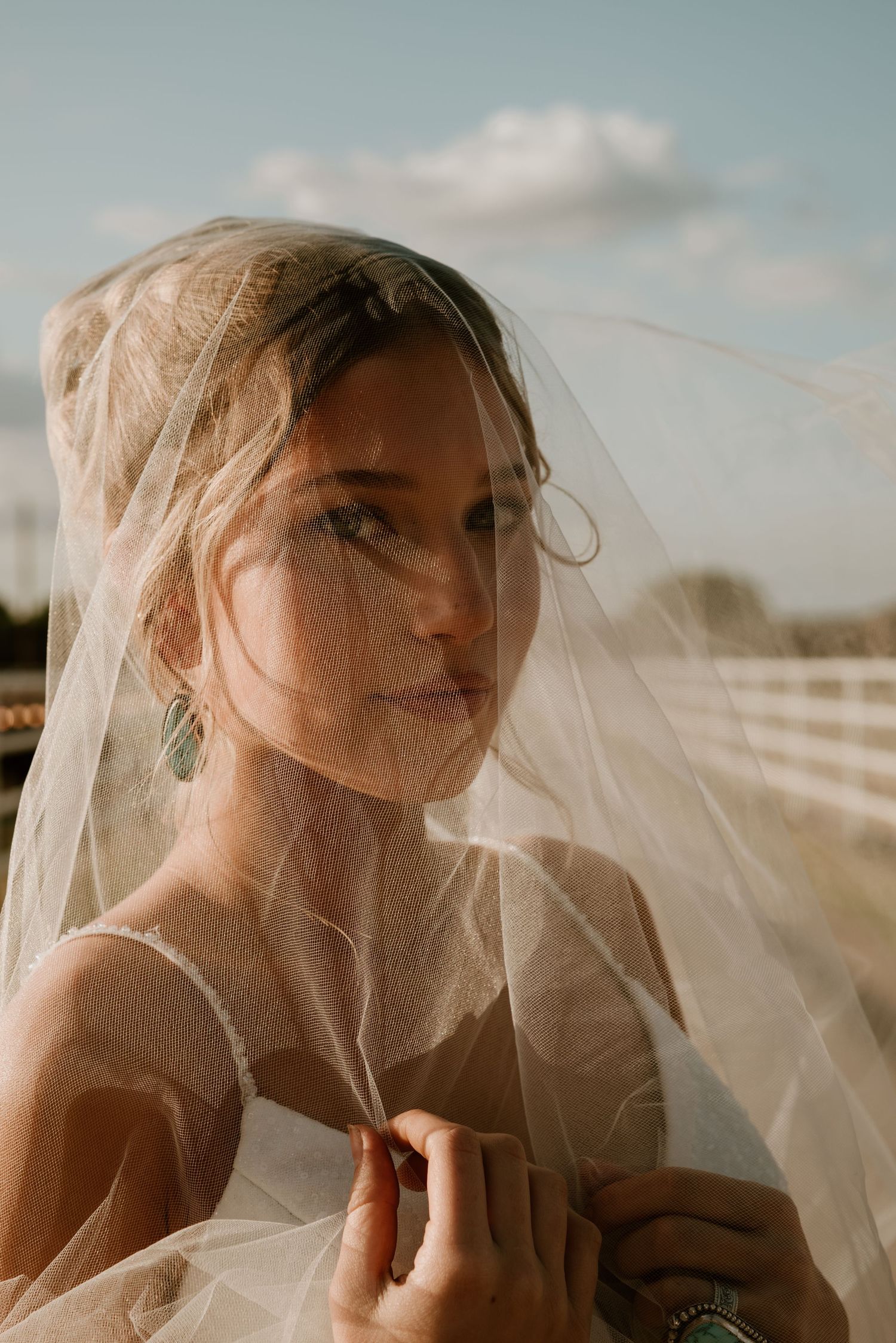 Ethereal bridal portrait with flowing veil against soft sky background.