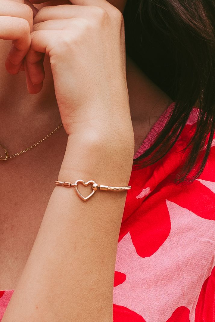 Delicate gold heart bracelet worn with red floral dress detail.