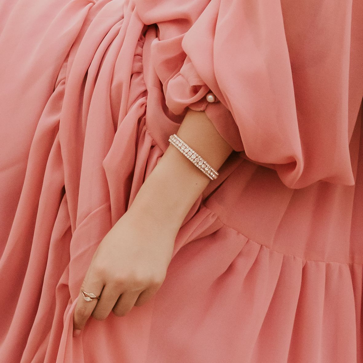 Close-up of an arm wearing a sparkly bracelet against flowing pink fabric.
