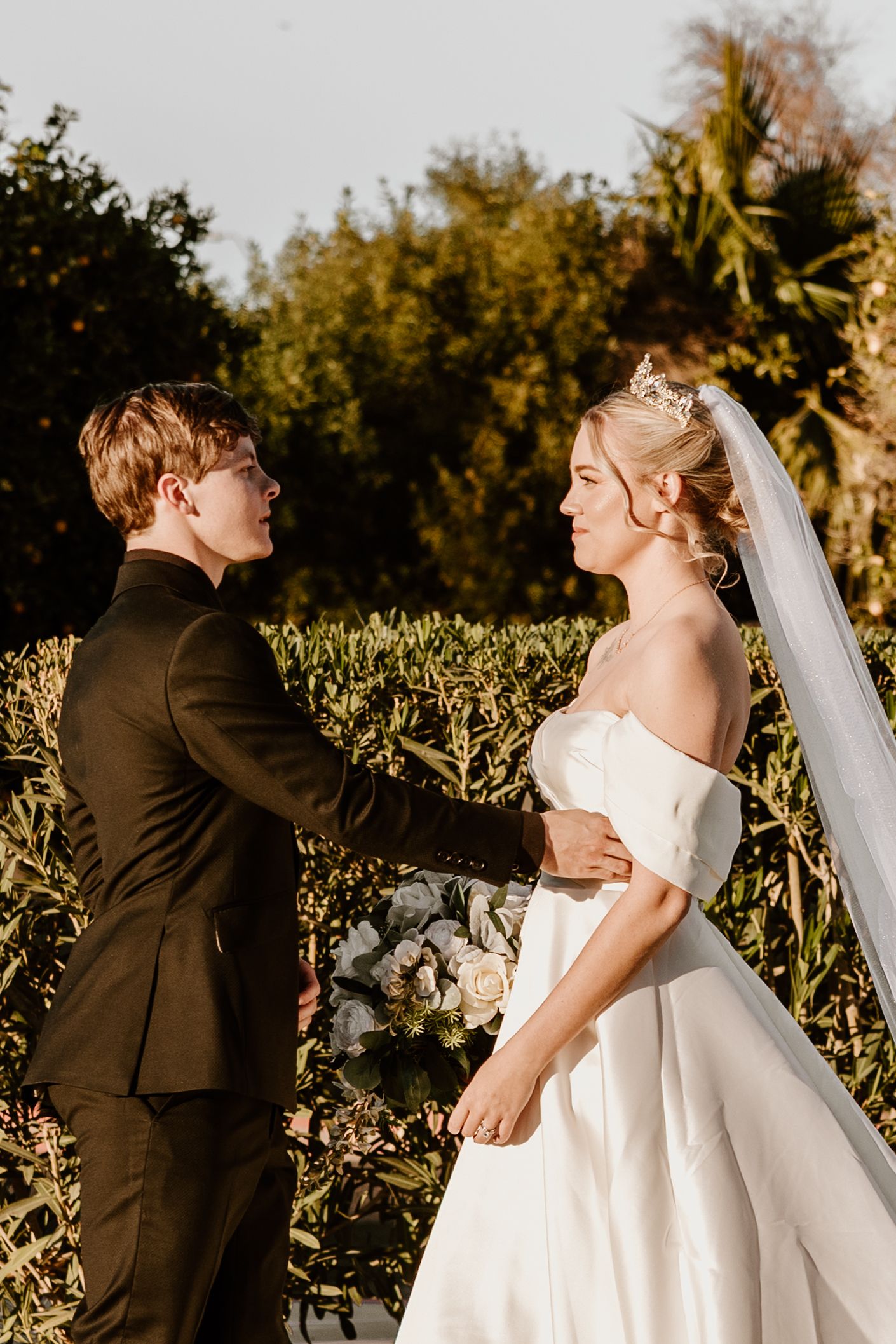 A romantic outdoor wedding portrait at golden hour with a bride in white and groom in dark attire.
