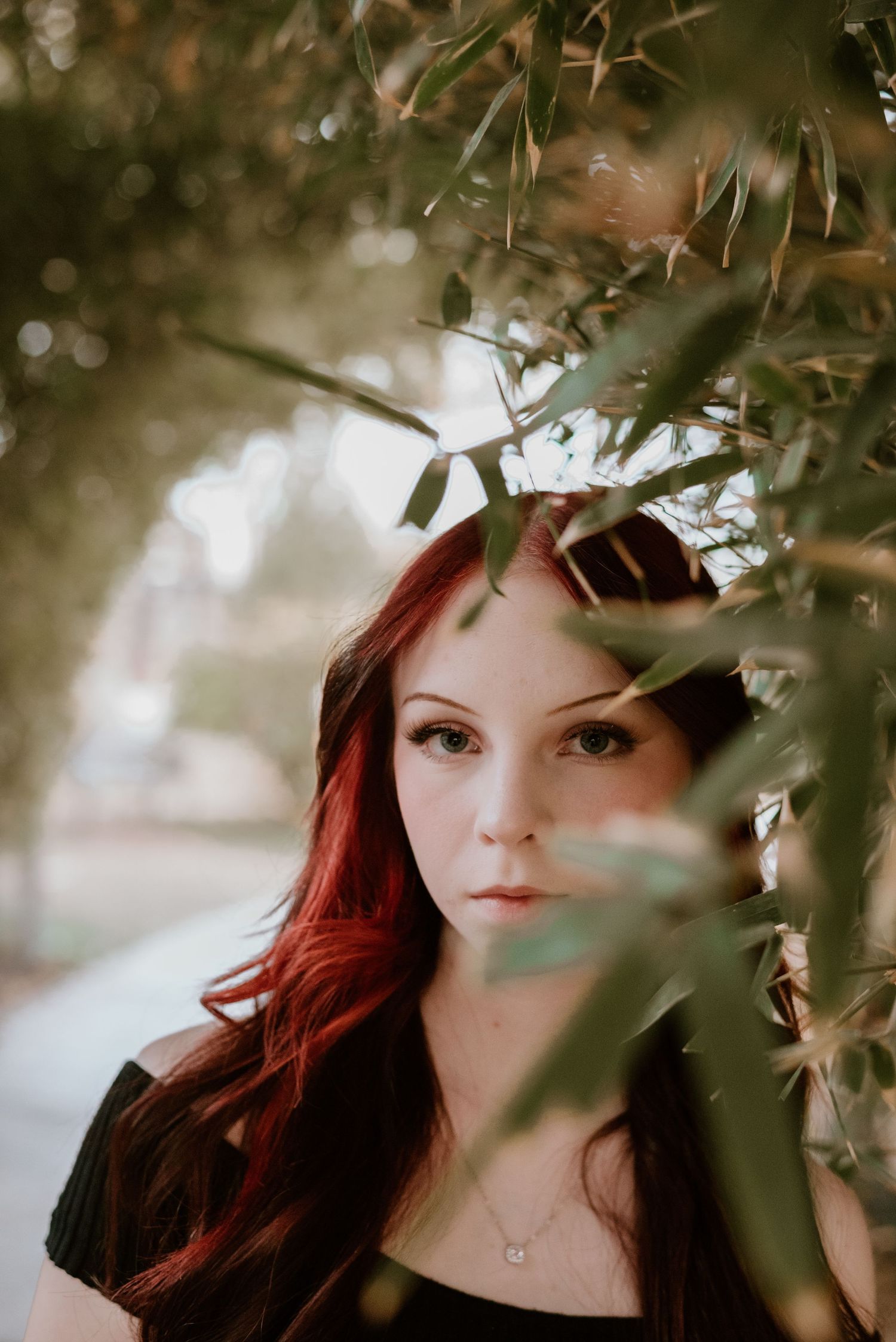 Artistic portrait through leaves and branches with moody lighting.