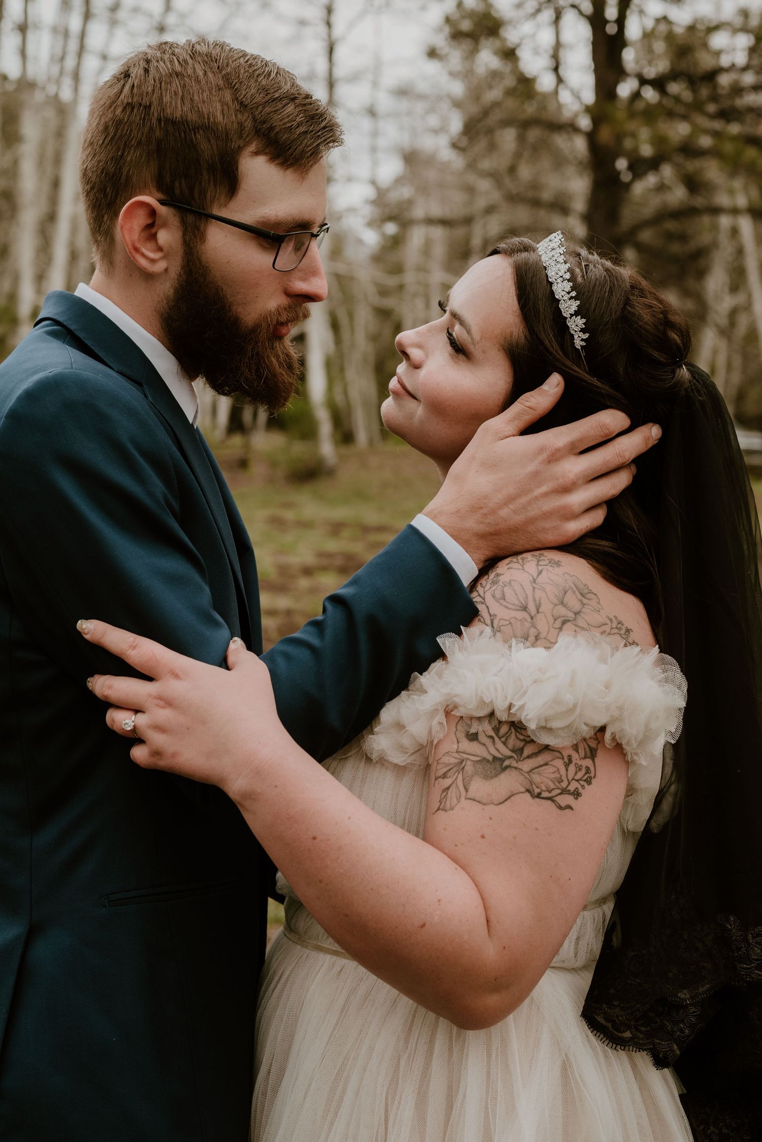 A tender wedding moment captured in a forest setting with elegant formal attire and natural lighting.