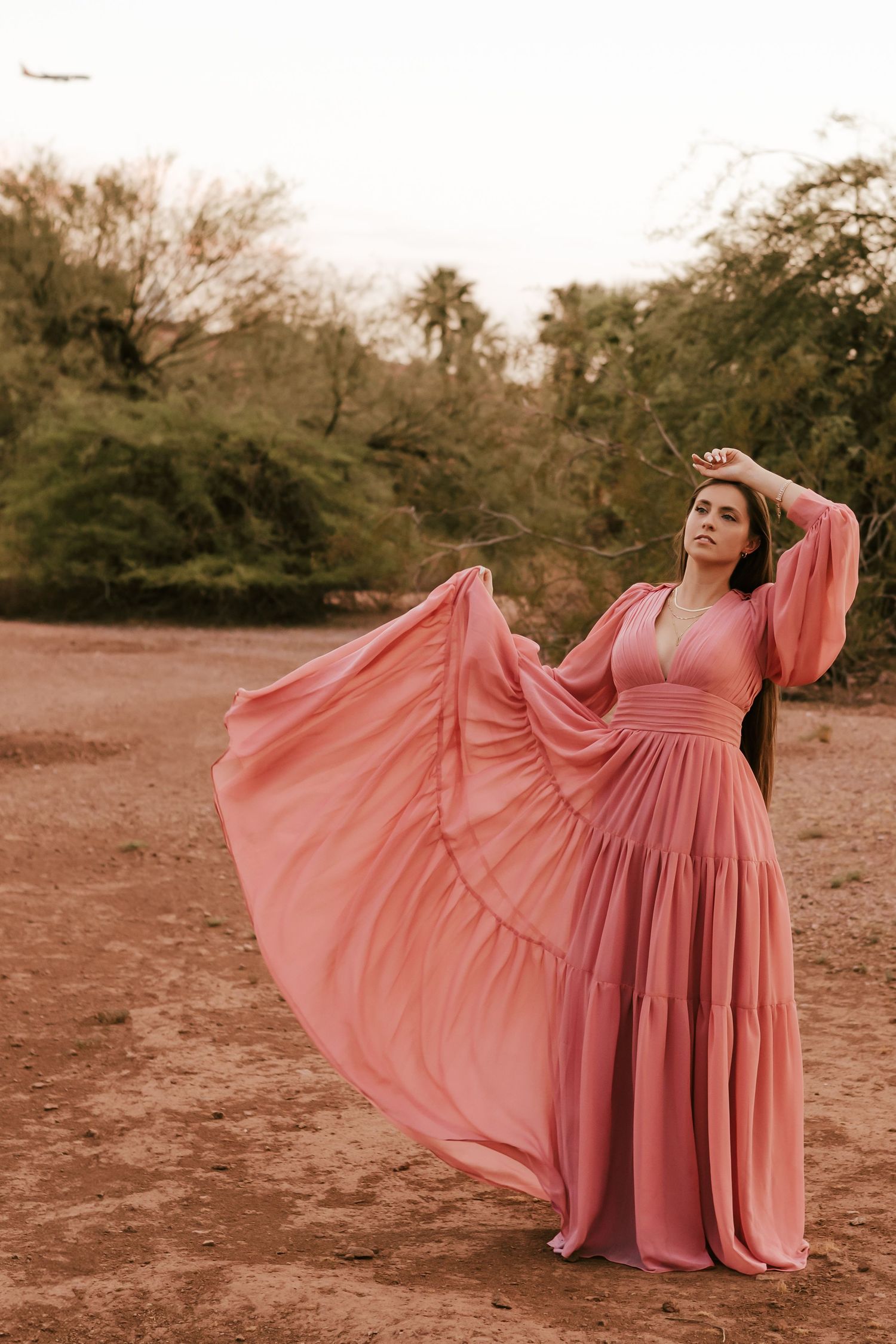 Flowing pink dress twirls gracefully in desert landscape during photoshoot.