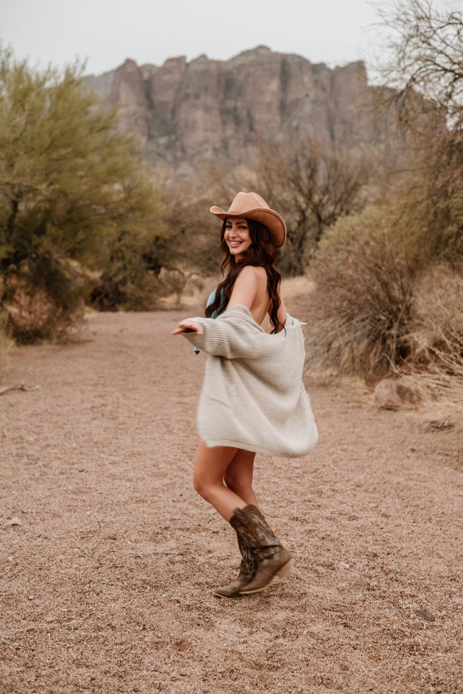 Playful desert fashion shot in oversized sweater, cowboy boots and western hat.