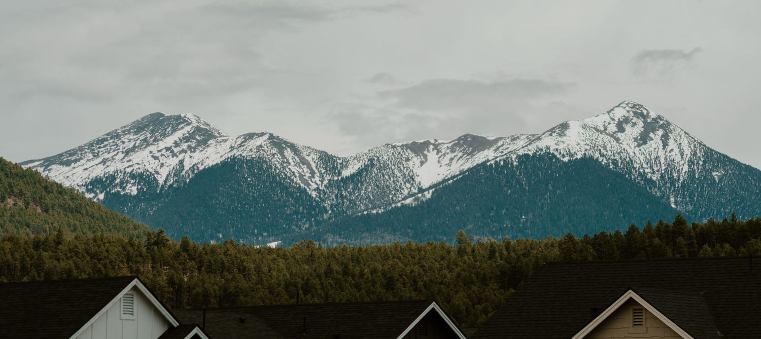 Snow-capped mountain peaks rise behind residential rooftops in a scenic valley.